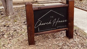 A building with a black door, two black chairs, and a sign that reads "The Church House Jefferson".