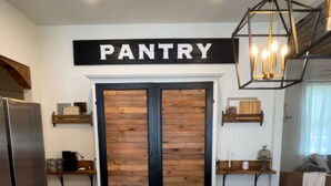 A kitchen with a marble countertop, wooden flooring, a 'PANTRY' sign above a double door, and a hanging light fixture.