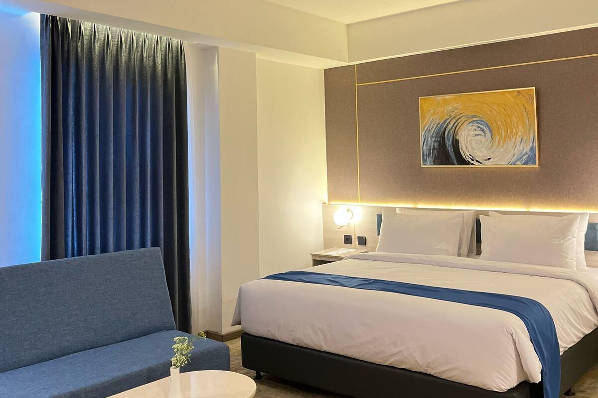 A hotel room with a bed, a sofa, a small table, and a painting on the wall.