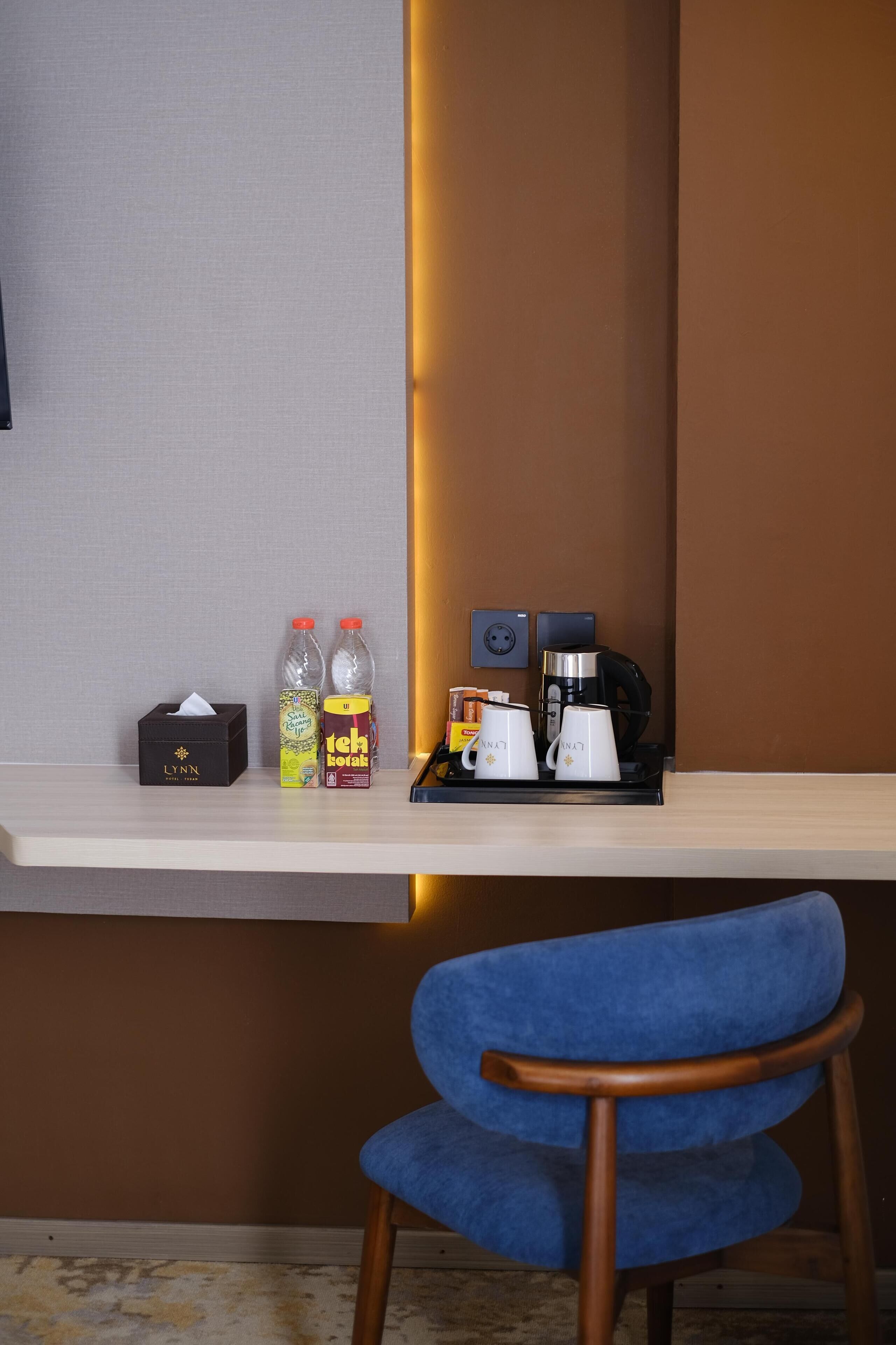Mostrador de recepción de hotel con una caja de pañuelos, dos botellas de agua, una caja de té, dos tazas blancas y una cafetera.