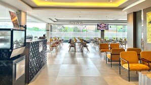 A modern restaurant with a long counter, yellow chairs, and a TV screen. - LYNN Hotel Tuban (Tuban)