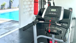A treadmill in a modern gym with a view of a swimming pool. - LYNN Hotel Tuban (Tuban)