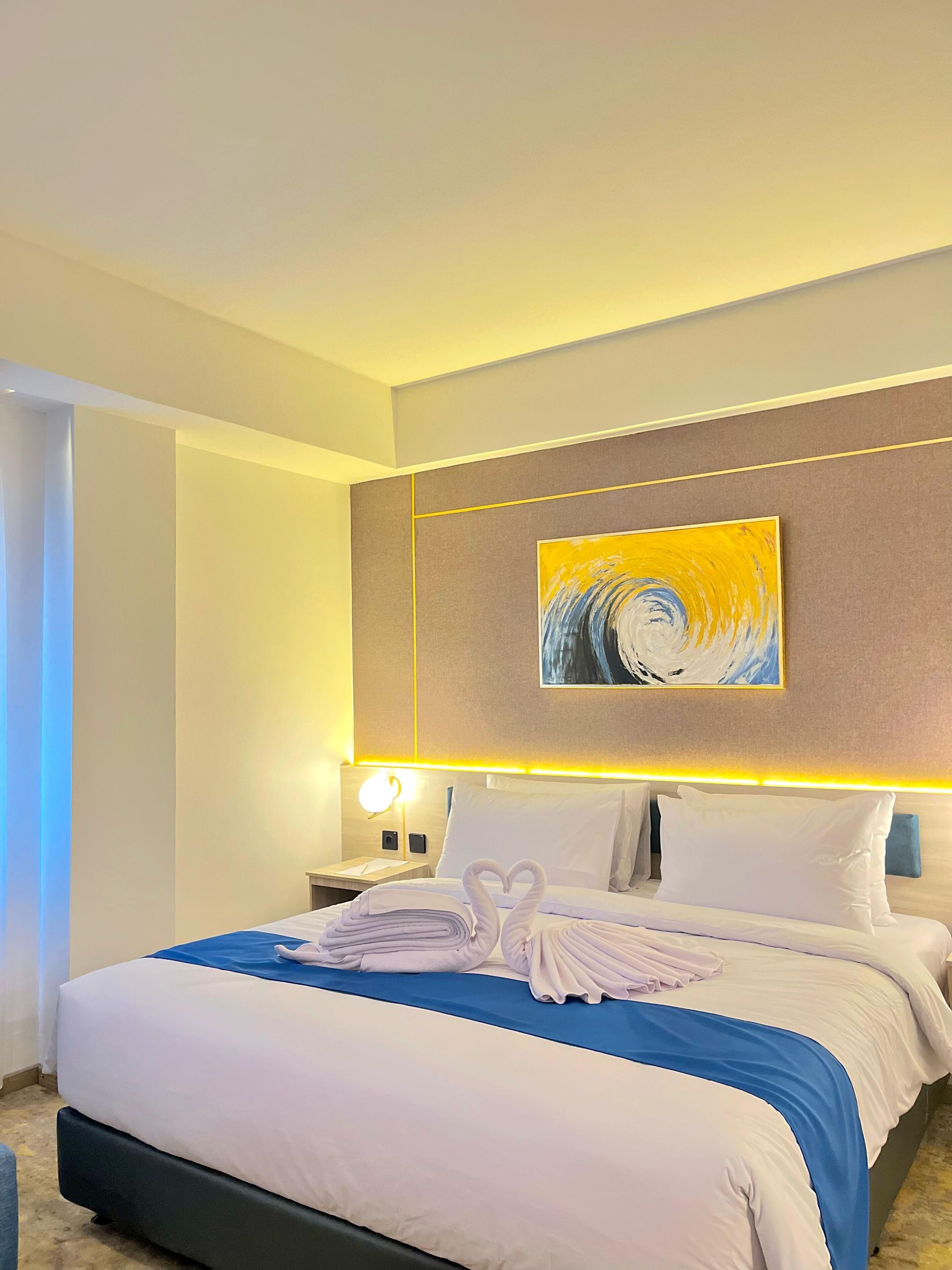 Una habitación de hotel con una cama bien hecha, un cuadro en la pared y una mesita de noche con una lámpara.