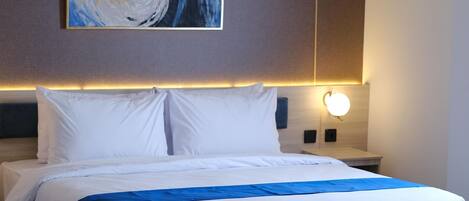 A hotel room with a large bed, a wall-mounted artwork, a bedside table with a lamp, and a carpeted floor.