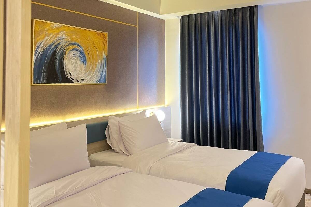 A hotel room with two beds, a painting on the wall, and a window with curtains.
