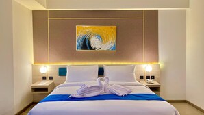 A hotel room with a large bed, two bedside tables, a wall-mounted painting, and a blue accent wall. - LYNN Hotel Tuban (Tuban)