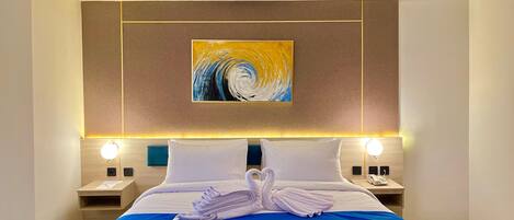 A hotel room with a large bed, two bedside tables, a wall-mounted painting, and a blue accent wall.