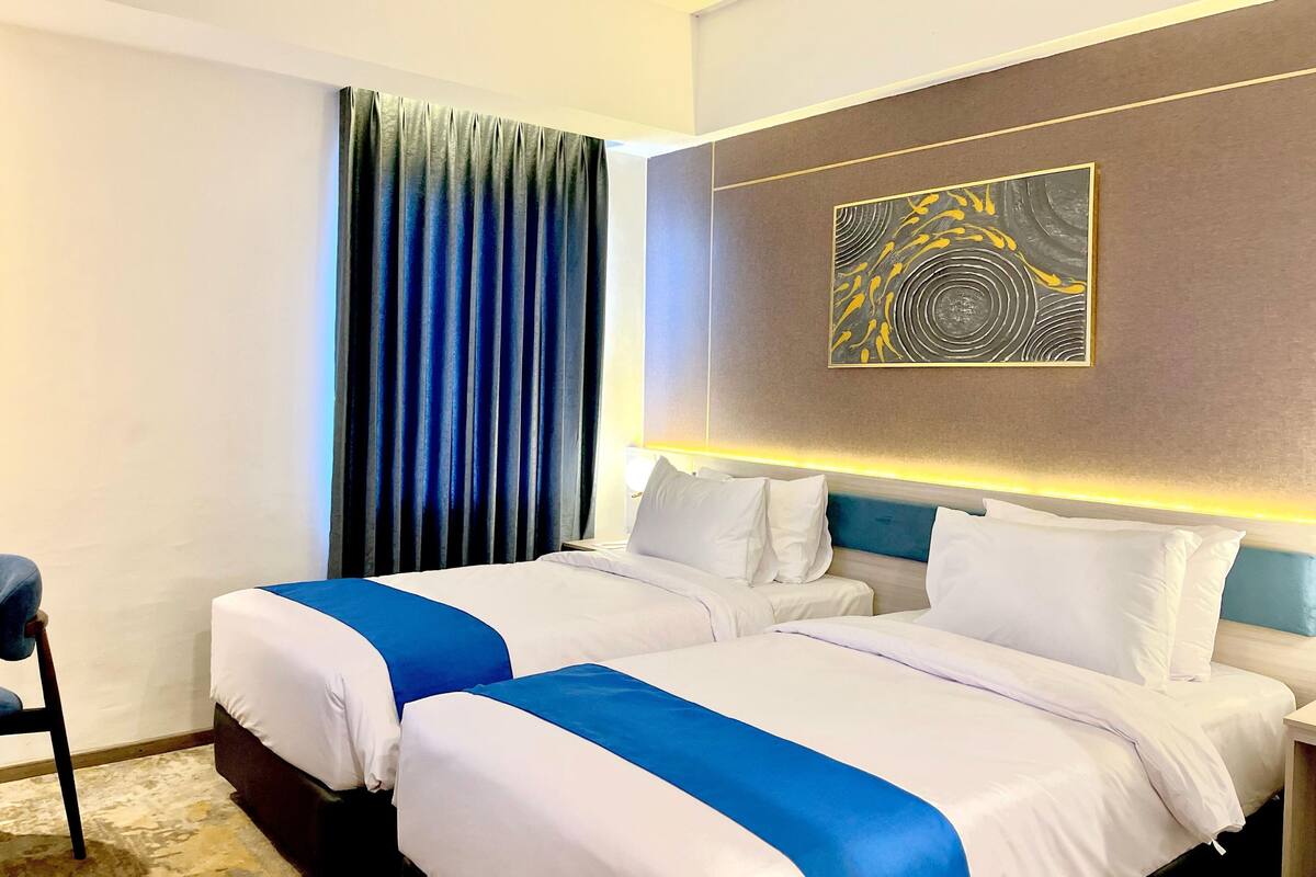 A hotel room with two beds, a large abstract painting on the wall, and a blue curtain.