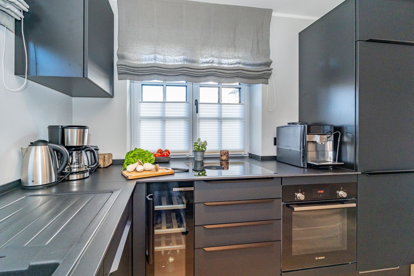 A modern kitchen with stainless steel appliances, a built-in oven, and a window with blinds.
