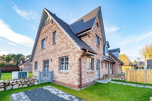 Une maison à deux étages, construite en briques, avec un toit en pente et un petit porche à l’avant.