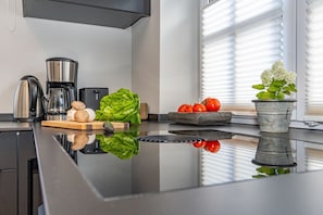 Eine moderne Küche mit glänzender Arbeitsplatte, einem Wasserkocher, einer Kaffeemaschine, frischem Gemüse und einer Topfpflanze.