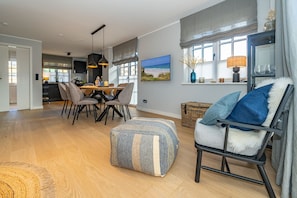 Un vaste espace de vie comprenant une table à manger, des chaises et un coin salon confortable avec un fauteuil et un pouf.