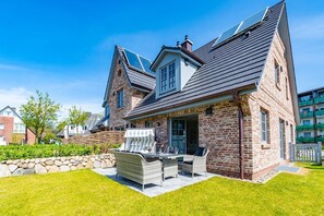A two-story house with a stone facade, a sloped roof, and a patio with outdoor furniture.