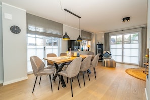 Un espace de salle à manger moderne avec une table en bois, des chaises à revêtement gris et des luminaires suspendus.