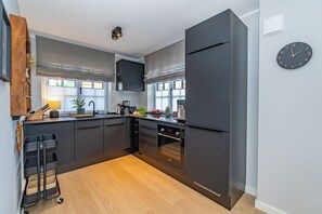 Une cuisine moderne avec des meubles de rangement aux couleurs sombres, un four encastré et une horloge murale.