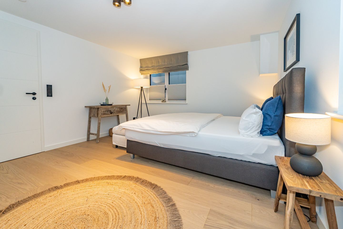 A bedroom with a bed, bedside lamp, wooden nightstand, and a small table with a lamp.