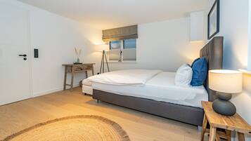 A bedroom with a bed, bedside lamp, wooden nightstand, and a small table with a lamp.
