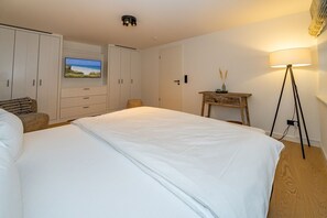 Une chambre avec un grand lit, un bureau avec une lampe et un téléviseur diffusant une scène de plage.