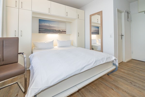 A bedroom with a bed, a chair, a wardrobe, and a mirror.