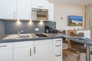 Uma cozinha moderna com forno embutido, pia e cafeteira. Há uma área de refeições com mesa e cadeiras.
