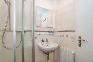 Une salle de bain moderne avec une douche à parois de verre, un lavabo blanc et un miroir au-dessus.