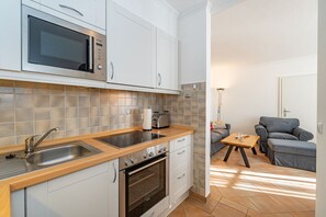 Une cuisine compacte équipée d’un four à micro-ondes, d’une cuisinière et d’un évier. Un petit coin repas avec une table et des chaises est également disponible.