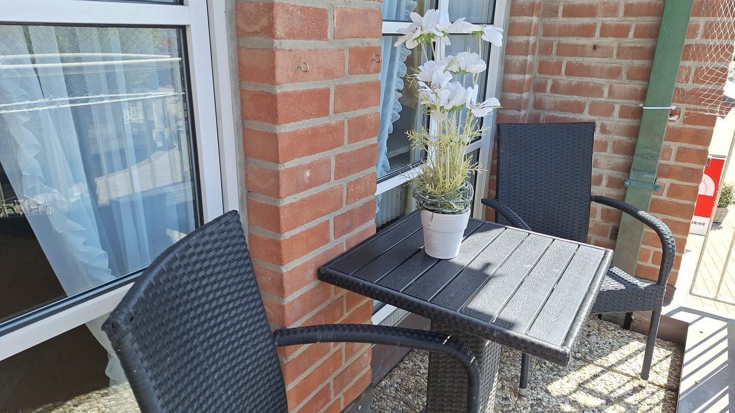 Ein kleiner Außenbereich mit Tisch und zwei Stühlen, einem Blumentopf und einer Glastür.
