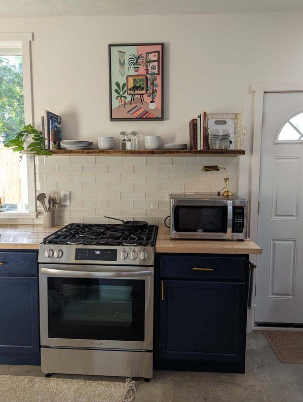 Cocina con estufa a gas, horno, microondas y encimera de madera.