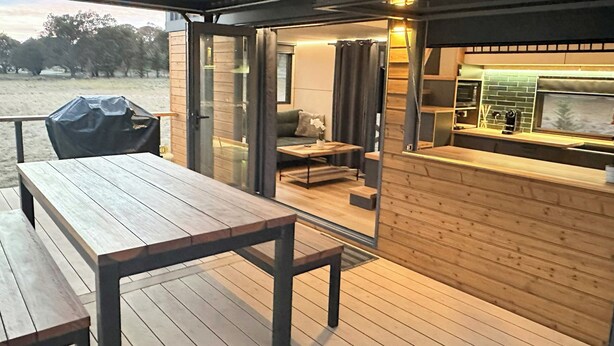 An outdoor patio area with a wooden table and benches, a grill, and a kitchen counter with a coffee machine.
