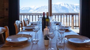 Une table à manger dressée pour un repas, avec vue sur des montagnes enneigées à travers de grandes fenêtres.
