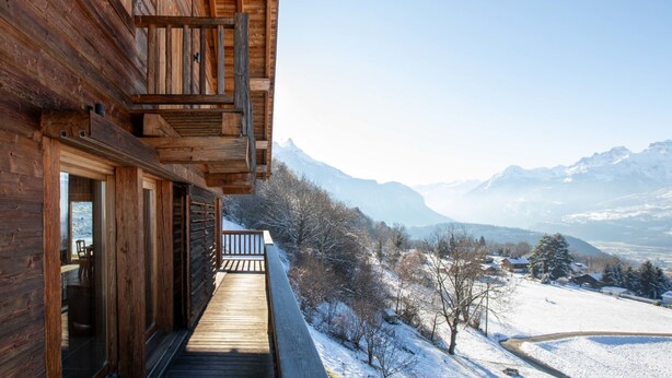 Une cabane en bois dotée d’un balcon donnant sur un paysage enneigé et des montagnes.