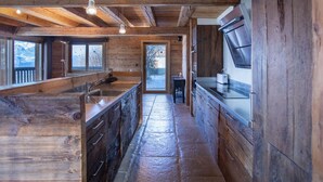 Une cuisine rustique dans une cabane en bois, avec un sol en pierre, des placards en bois et une grande fenêtre donnant sur un paysage enneigé.