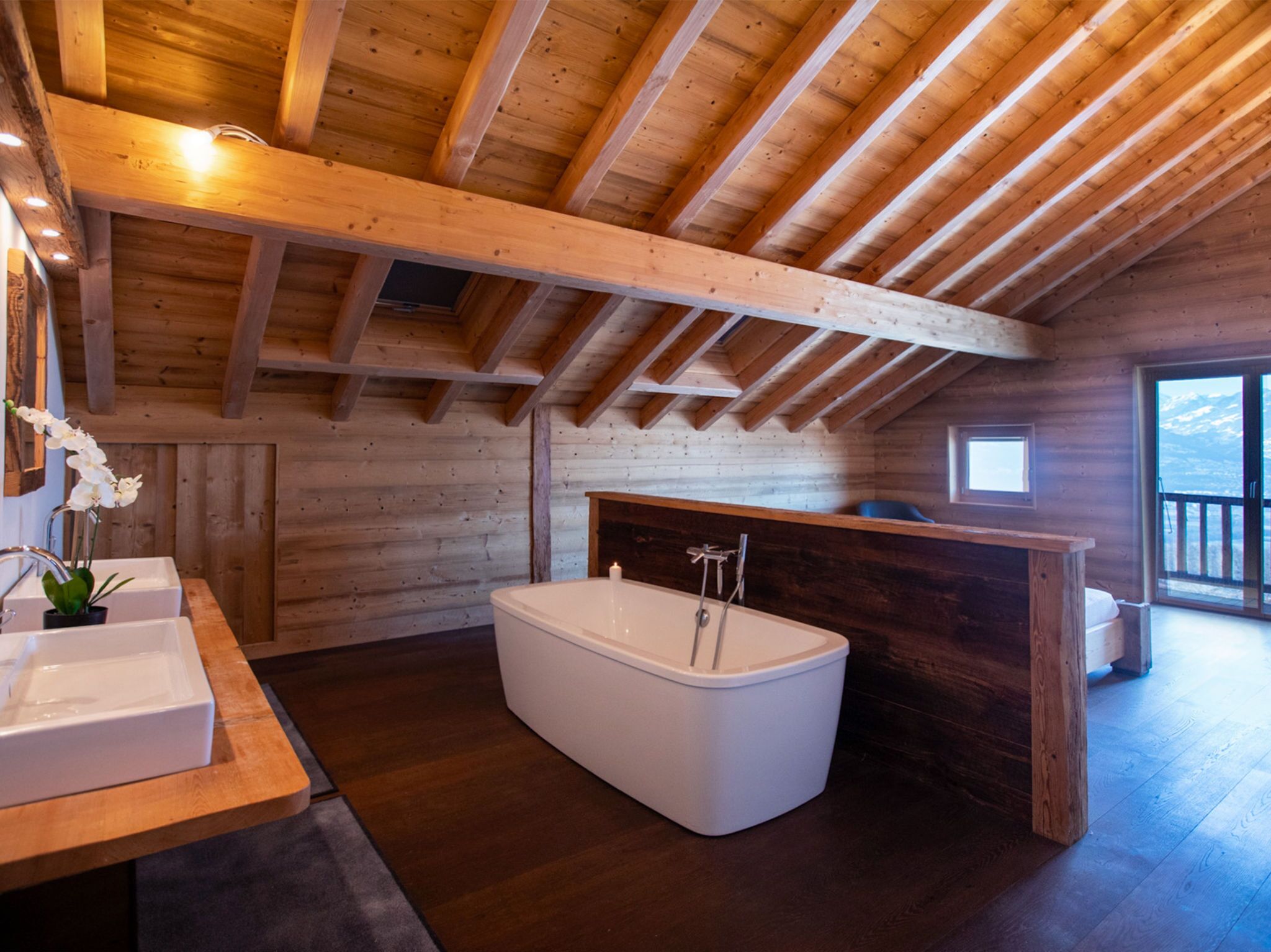 Interior de una cabaña de madera con baño que incluye una bañera, un lavabo y una ventana con vistas a las montañas.