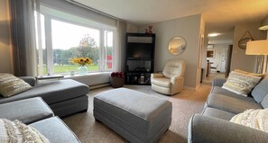 Relax in a serene space with a view of the lush outdoor area, featuring a comfortable seating area and flat-screen TV.