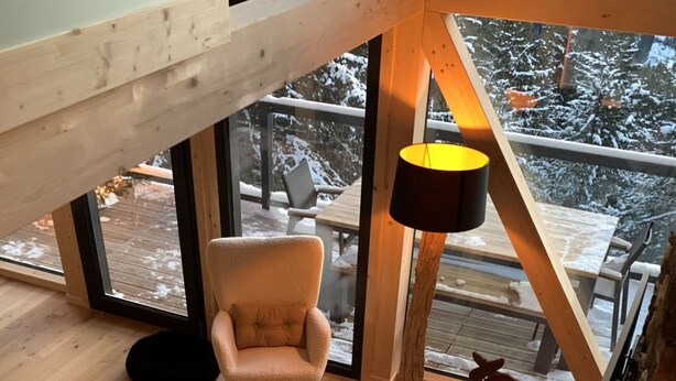 Tunnelmallinen sisustus, jossa on puulattia, harmaa sohva, pehmeä matto, puinen sohvapöytä ja suuri ikkuna, josta avautuu näkymä lumiseen maisemaan.