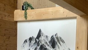 Huoneessa on suuri maalaus, jossa on kuvattuna vuoristomaisema, ja se on sijoitettu seinälle. Lisäksi huoneessa on puinen katto ja harmaa sohva.