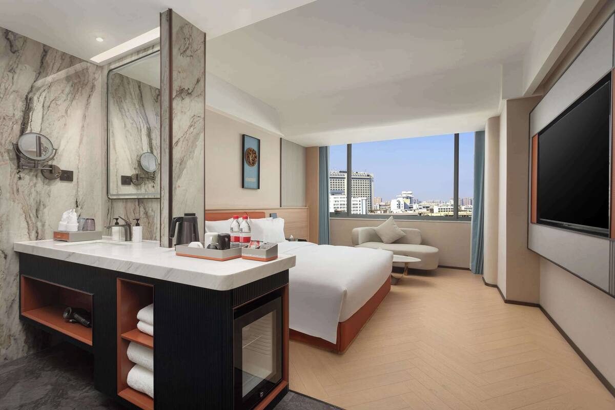 Ein modernes Hotelzimmer mit einem großen Bett, einer Sitzecke, einem großen Spiegel und einem Fernseher.