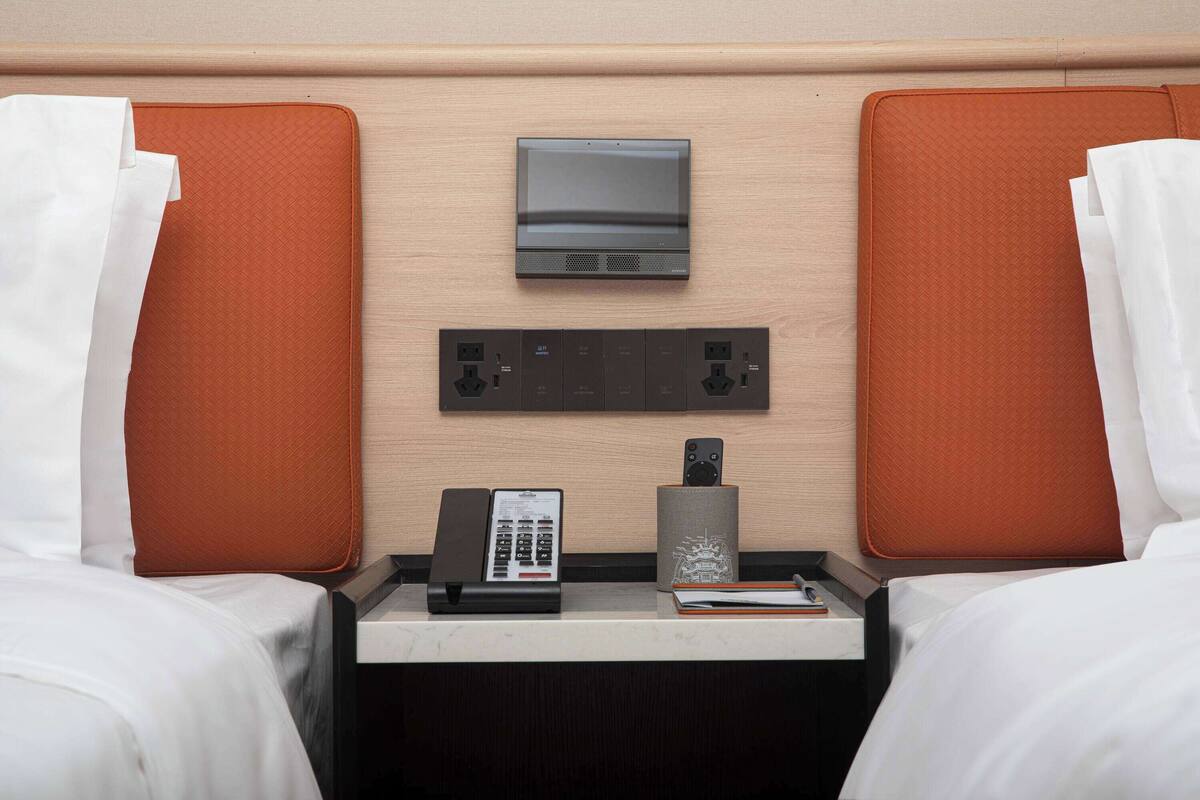 Ein Hotelzimmer mit zwei Betten, einem Fernseher, einem Telefon und einem kleinen Tisch mit einem Buch und einer Fernbedienung.