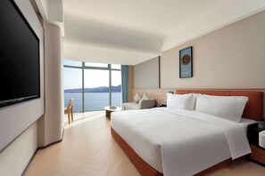 A hotel room with a large bed, a TV mounted on the wall, a small table, and a view of the sea. - Days Inn by Wyndham Shantou Jinping (Shantou)