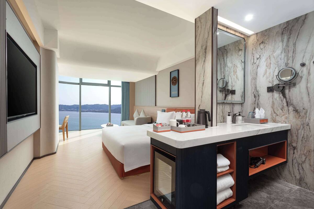 Ein modernes Hotelzimmer mit einem großen Bett, einem Badezimmer mit Marmorwaschtisch und Blick aufs Meer.