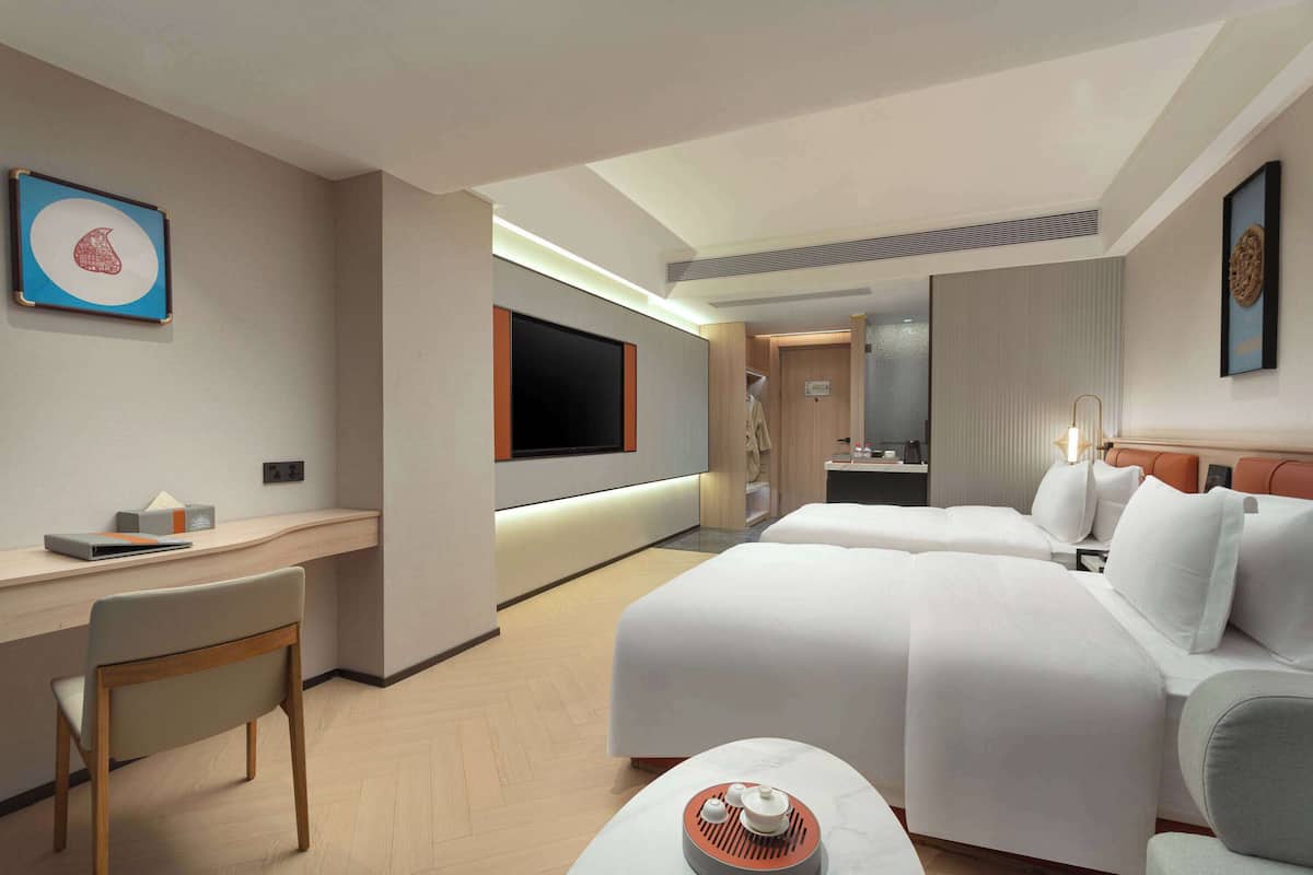 Ein Hotelzimmer mit Schreibtisch, zwei Betten, Fernseher und Bad.