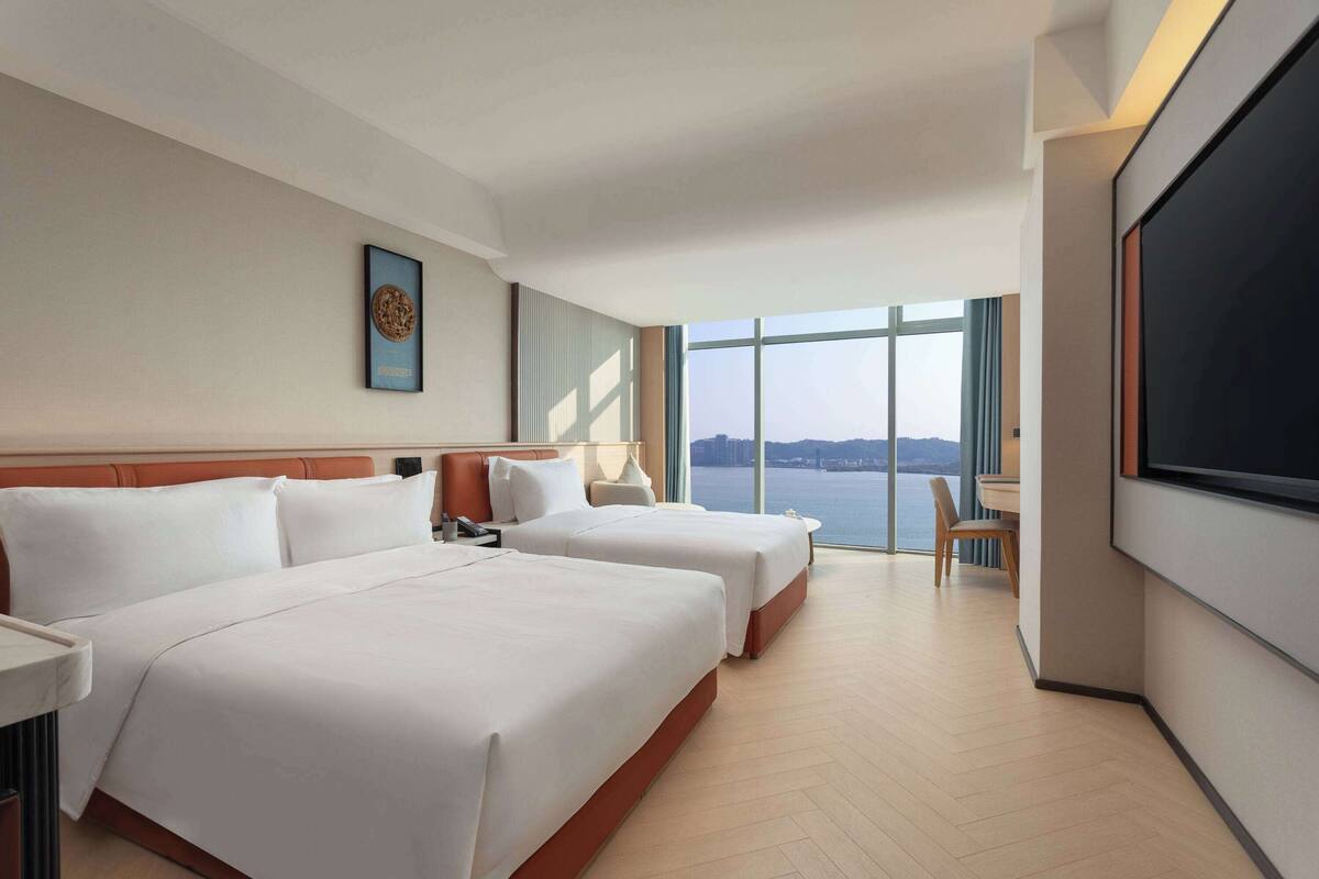 Ein Hotelzimmer mit zwei Betten, einem großen Fernseher und Blick auf das Wasser.