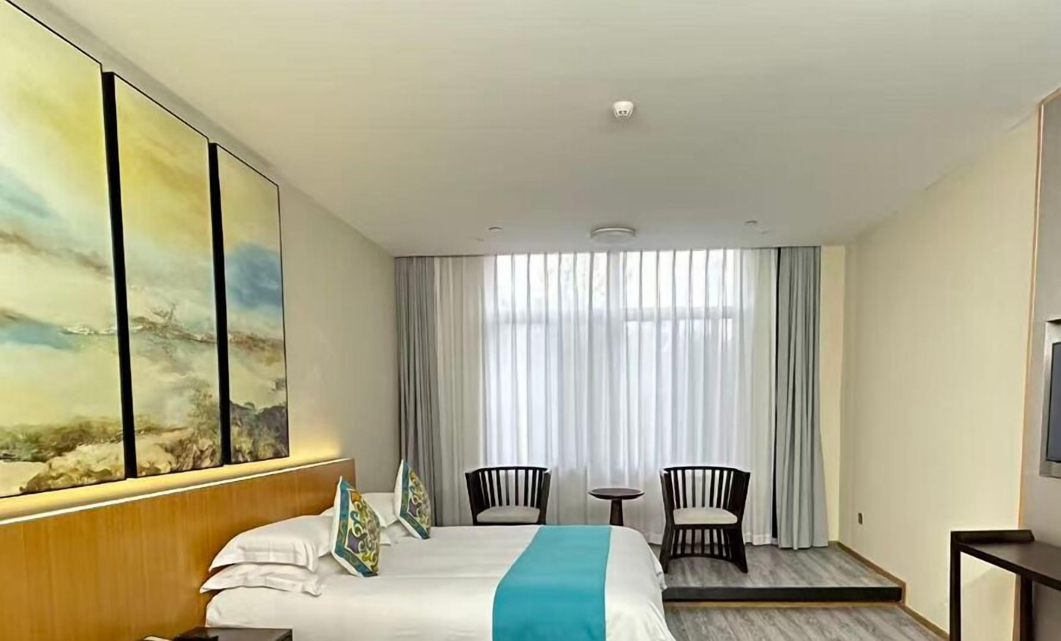 A hotel room with a large bed, two chairs, a small table, and a painting on the wall.