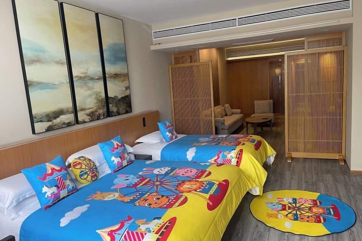 A hotel room with two beds, colorful bedding, a large window, and a view of the beach.