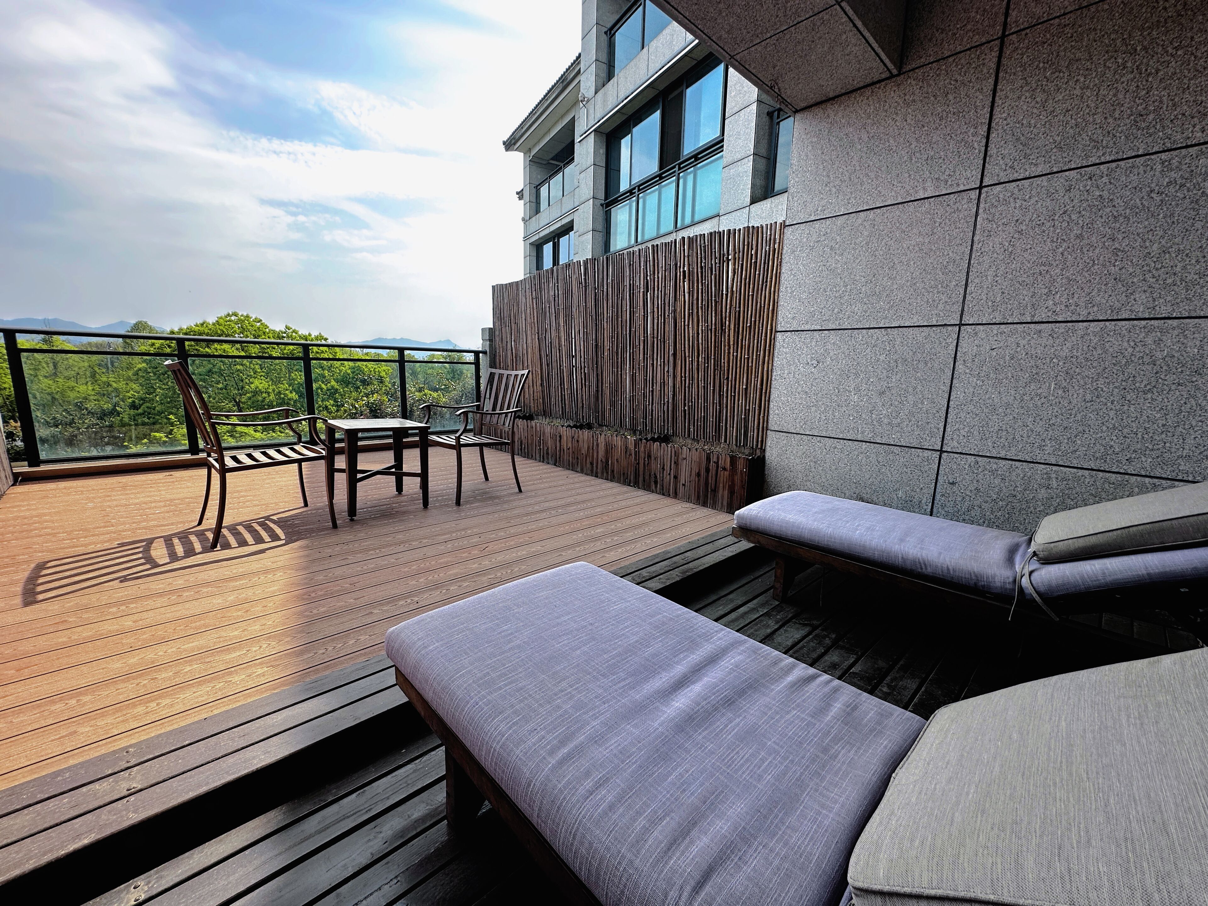 A wooden deck with a table and chairs, a cushioned bench, and a view of greenery and mountains.