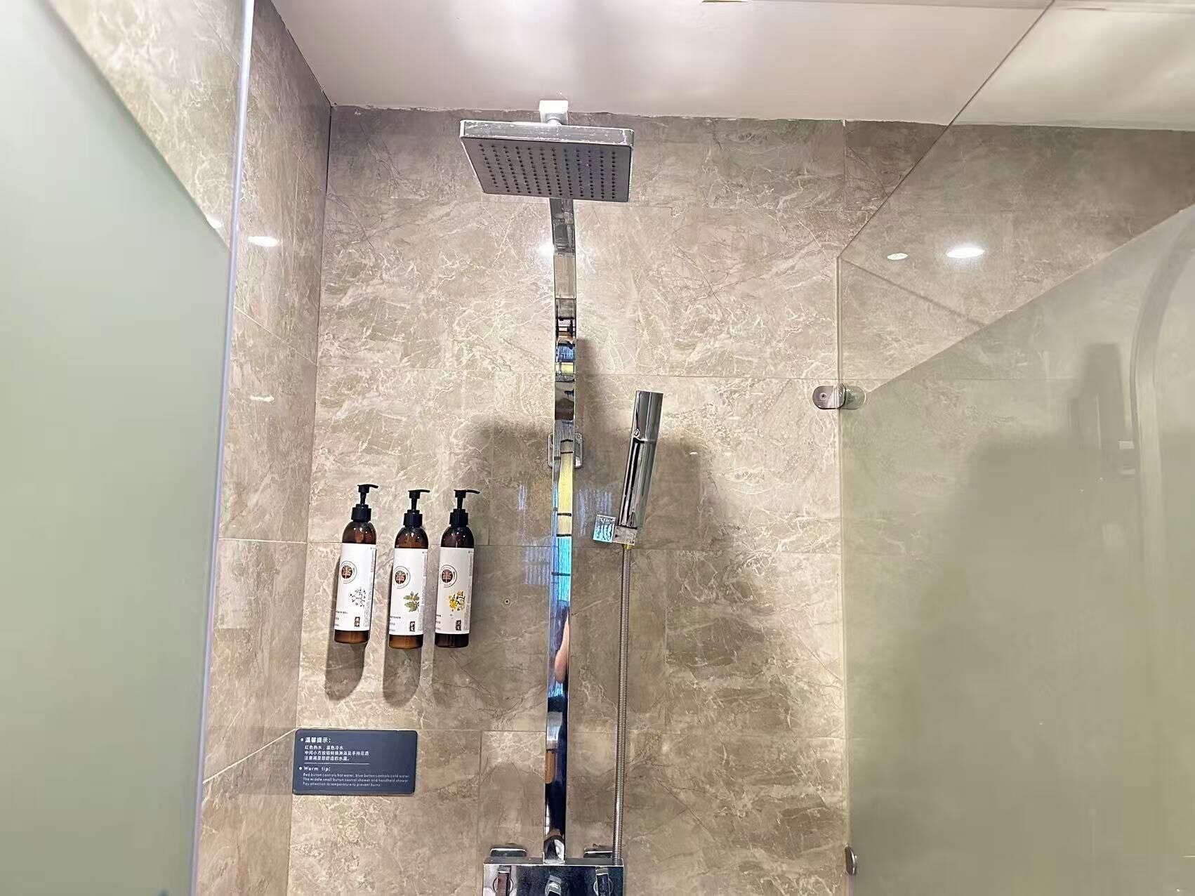 A modern bathroom with a glass-enclosed shower, a wall-mounted faucet, and three bottles of shampoo.