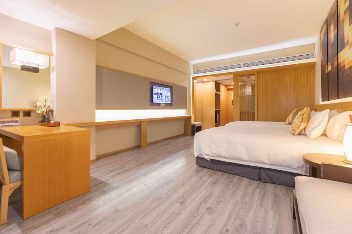 A hotel room with a bed, a desk, a television, and a wooden wardrobe.