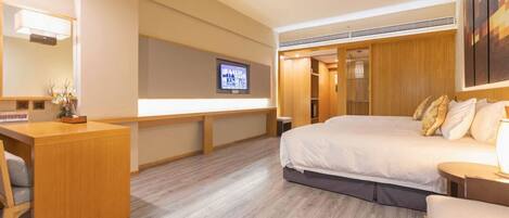 Quarto de hotel com cama, escrivaninha, televisão e guarda-roupa de madeira.