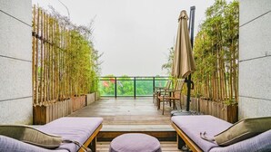 A balcony with two lounge chairs, a wooden table, and bamboo plants. - SSAW Boutique Hotel Hangzhou Xixi NanLu - Close to Xixi Wetland Area (Hangzhou)