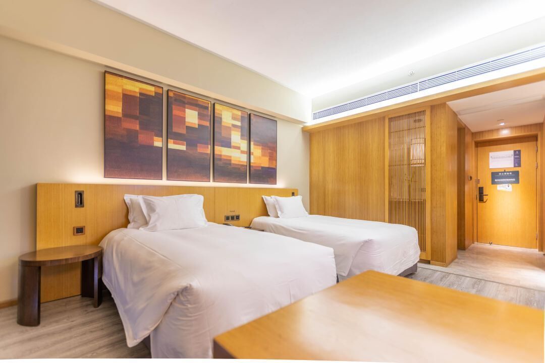 A hotel room with two beds, a wooden headboard, a nightstand, a wooden table, and a large abstract painting on the wall.